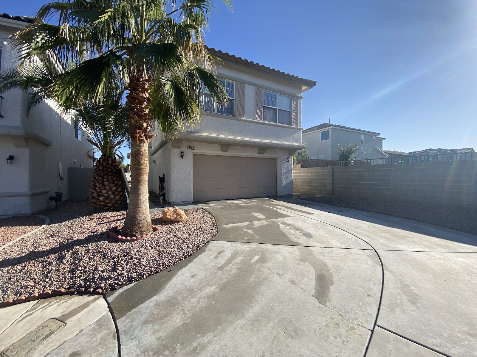 Two-story home with a clean concrete driveway and a palm tree under a blue sky
