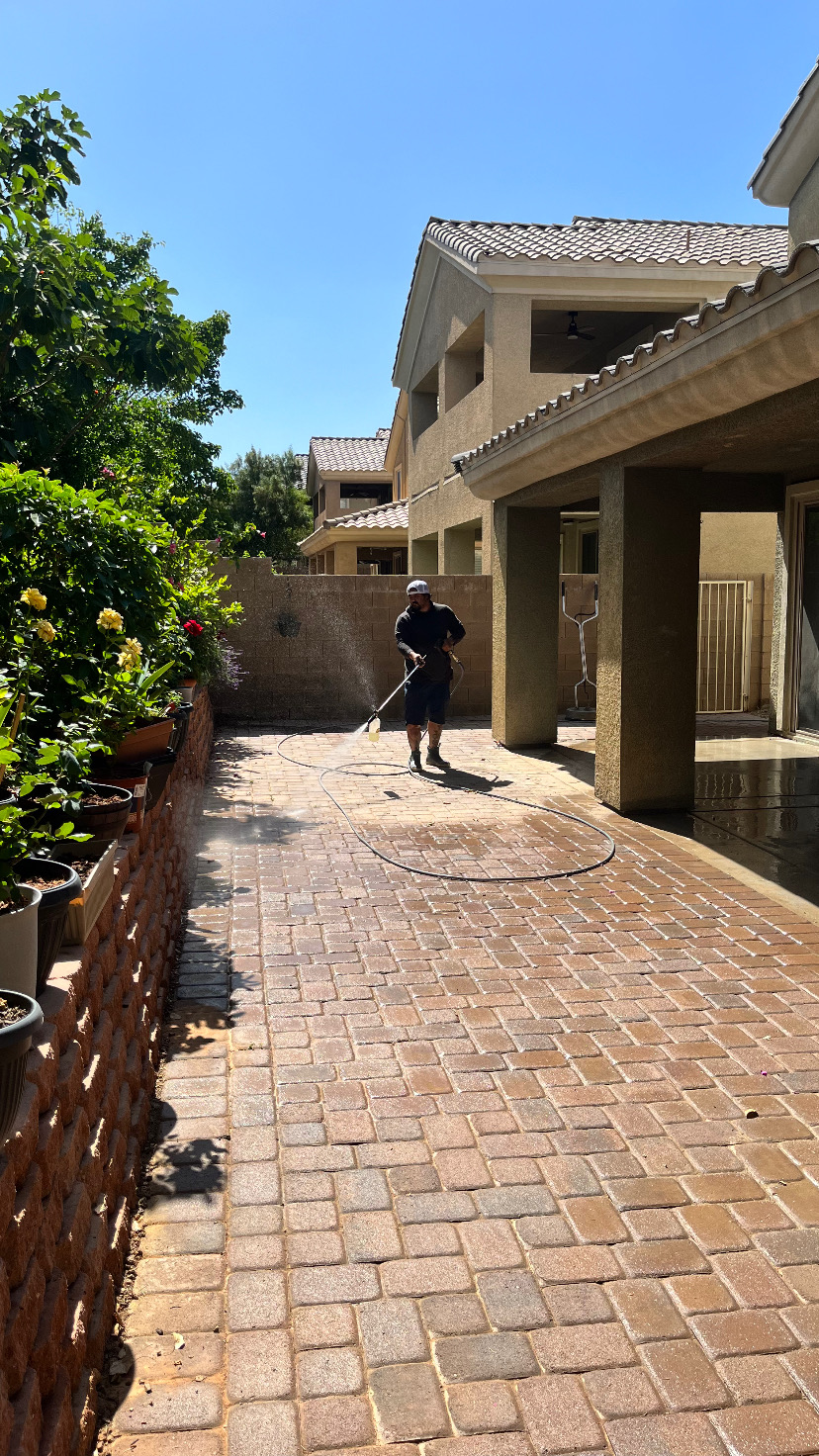 Worker pressure washing a paver walkway between homes on a sunny day